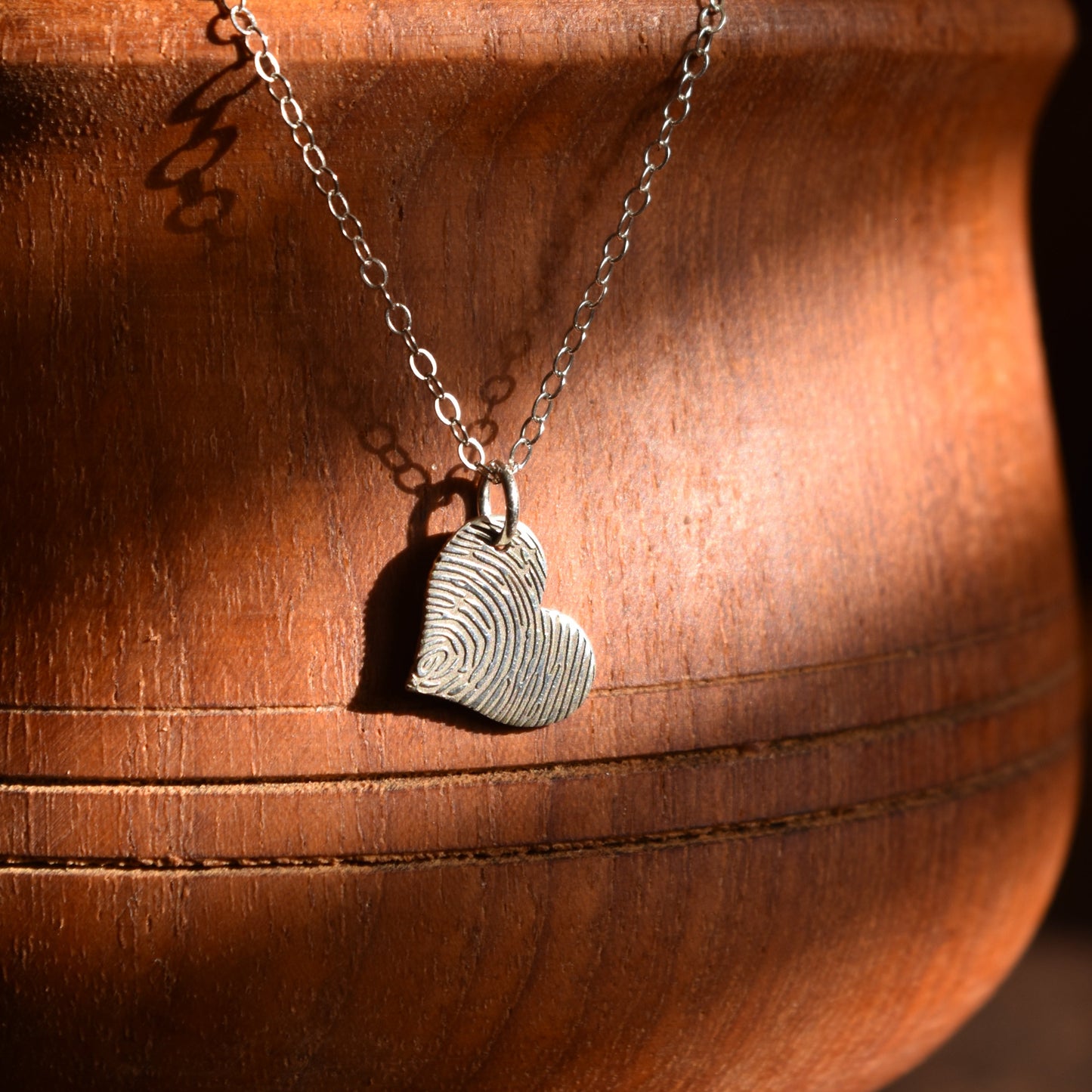 Necklace with a heart fingerprint pendant on a wooden surface. Personalised engraved jewellery. April Child